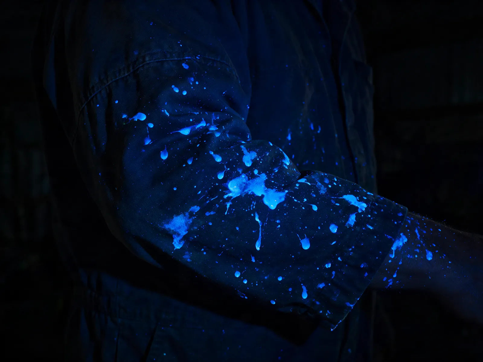 Macacão de operador sob luz negra com respingos fluorescentes azuis na manga